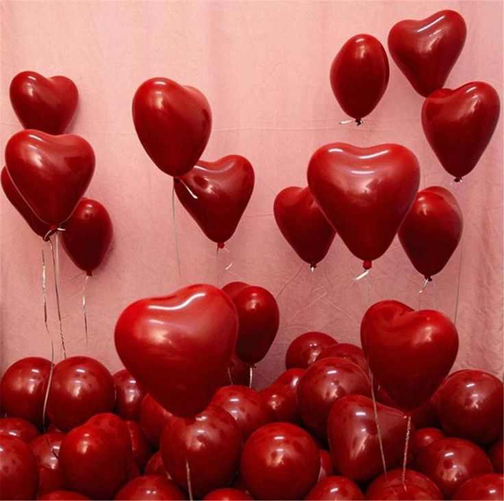 there are many red heart shaped balloons in the shape of hearts hanging from strings on a wall