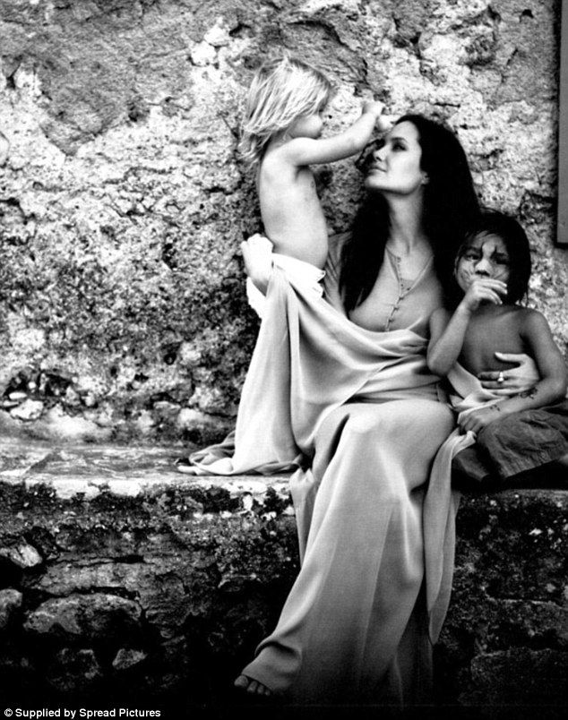 two women and a child sitting on a stone bench in front of a wall with graffiti