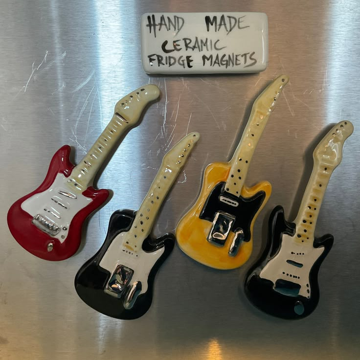 three miniature guitars are sitting on the refrigerator door, one is red and one is yellow