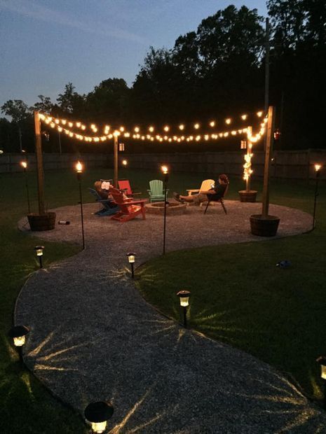 an outdoor patio with string lights and lawn chairs on the gravel path leading to it