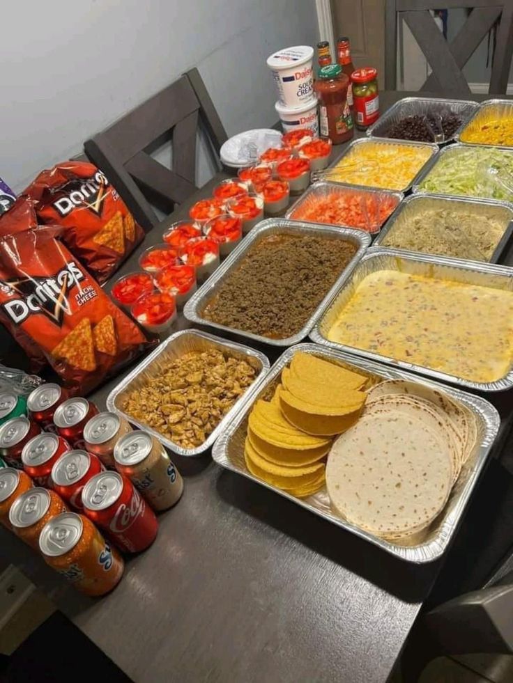 a table filled with lots of food on top of metal trays next to cans of soda