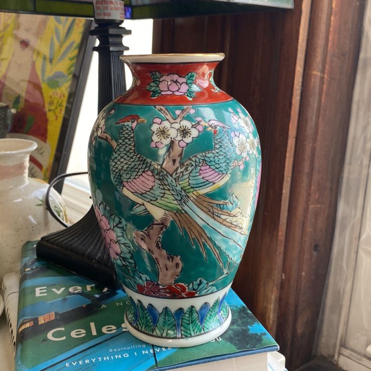 a vase sitting on top of a stack of books next to a lamp and other items