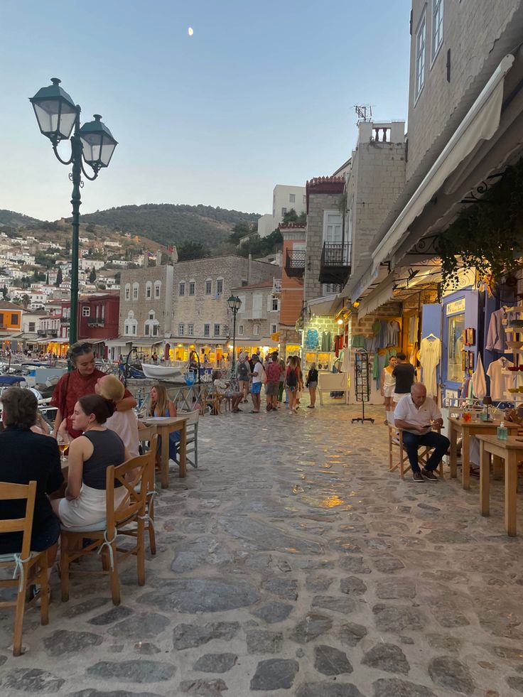 people are sitting at tables in the middle of an open air area with buildings on either side