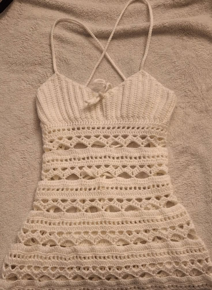 a white crocheted dress laying on top of a bed next to a pillow