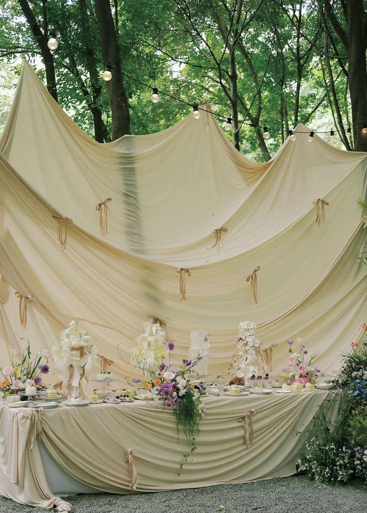 the table is set up with white flowers and cloth draped over it for an outdoor wedding reception