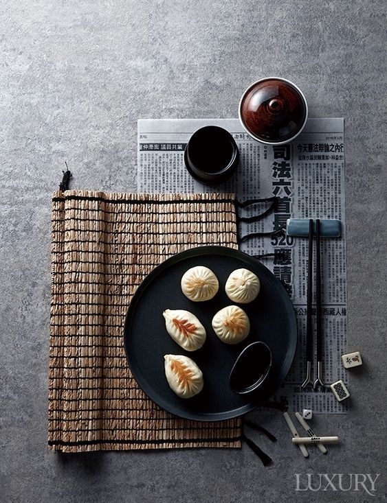 some food is on a black plate with chopsticks and saucers next to it