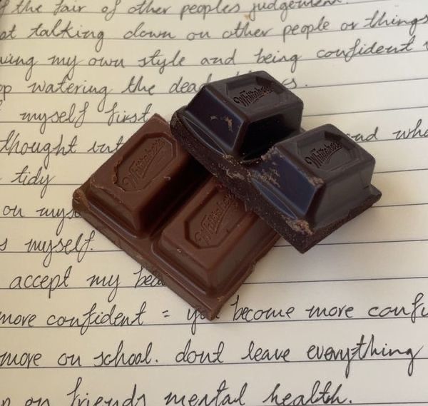 two pieces of chocolate sitting on top of a piece of paper with writing in the background