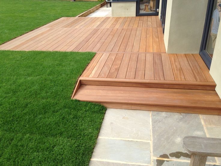 a wooden deck with steps leading up to the front door and grass in the back yard