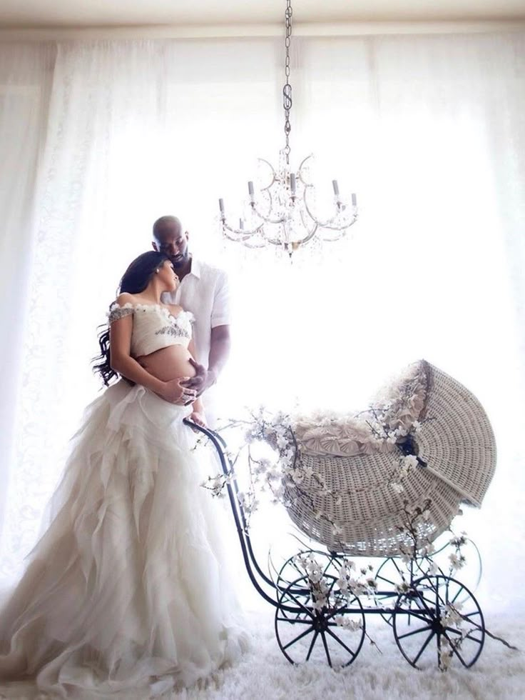 a man and woman standing next to a baby carriage in front of a chandelier