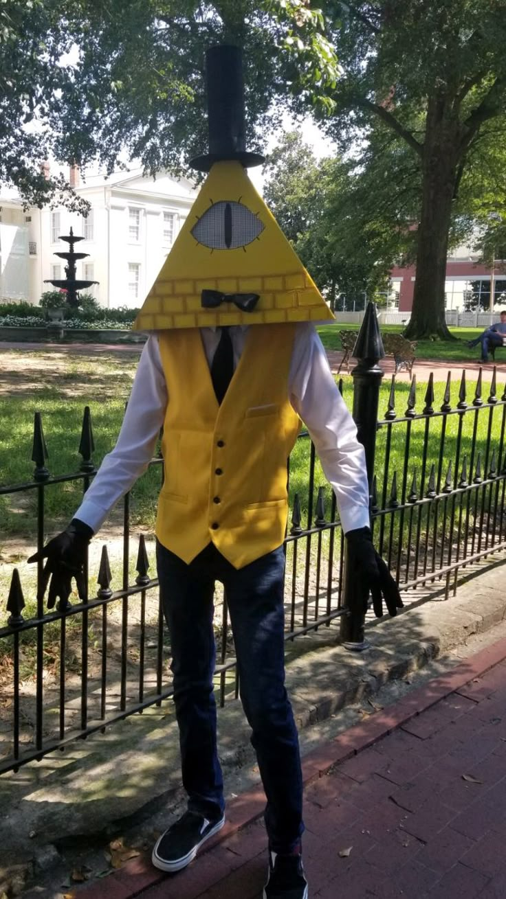 a man in a yellow vest and tie standing next to a fence with a banana mask on his head