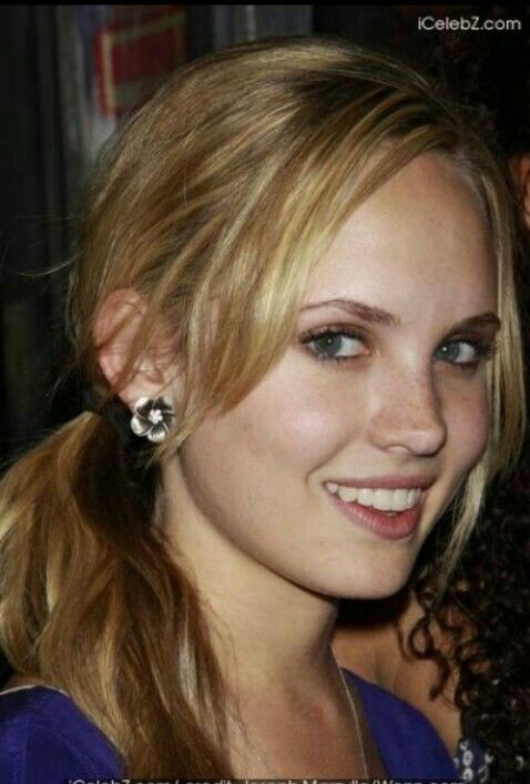 a close up of a person with blonde hair and blue eyes wearing earrings