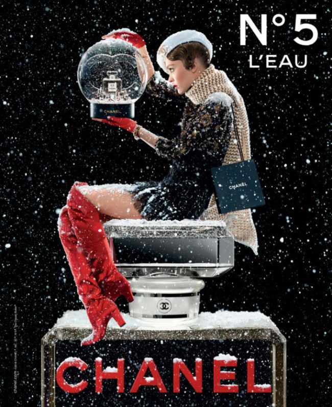 a woman in red boots sitting on top of a chanel sign with snow falling around her