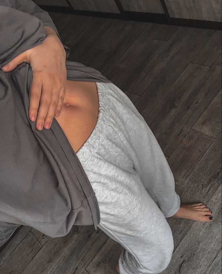 a woman laying on top of a bed covered in a gray blanket next to a wooden floor