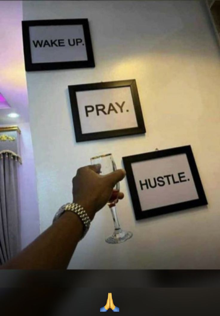 a person holding a wine glass in front of three framed signs on the wall that say wake up, pray, hustle