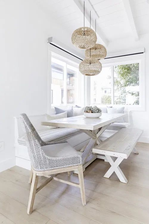 a dining room table and bench in front of a large window with two lamps hanging from the ceiling