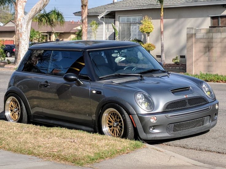 a small gray car parked on the side of a road next to a tree and house