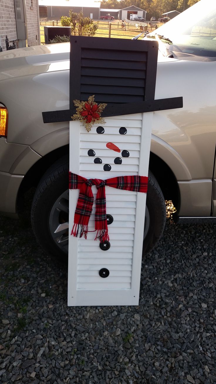 a snowman made out of shutters sitting next to a car