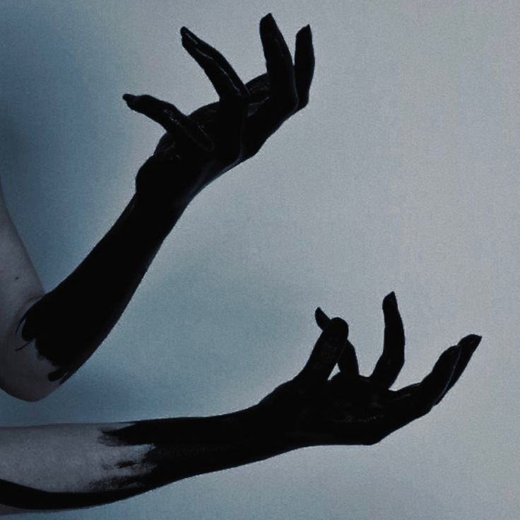 two hands reaching up towards each other with black and white paint on their arms, against a light blue background