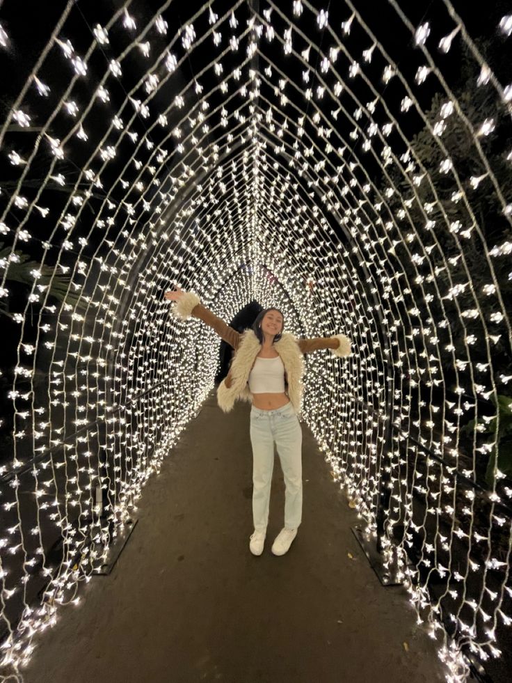 a woman standing in the middle of a tunnel covered with christmas lights