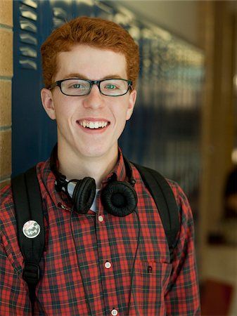 a young man with red hair wearing headphones and a plaid shirt smiles at the camera