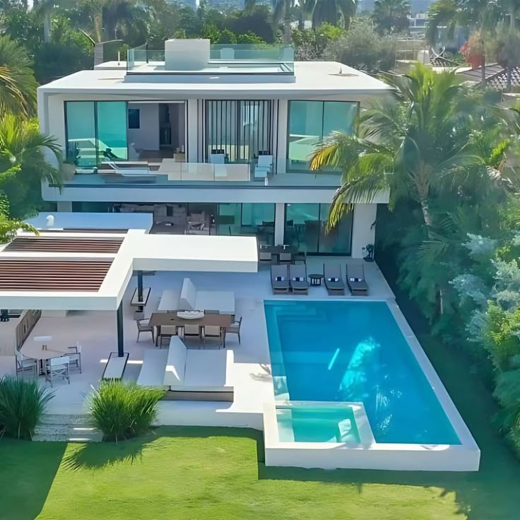 an aerial view of a house with a swimming pool in the foreground and palm trees surrounding it