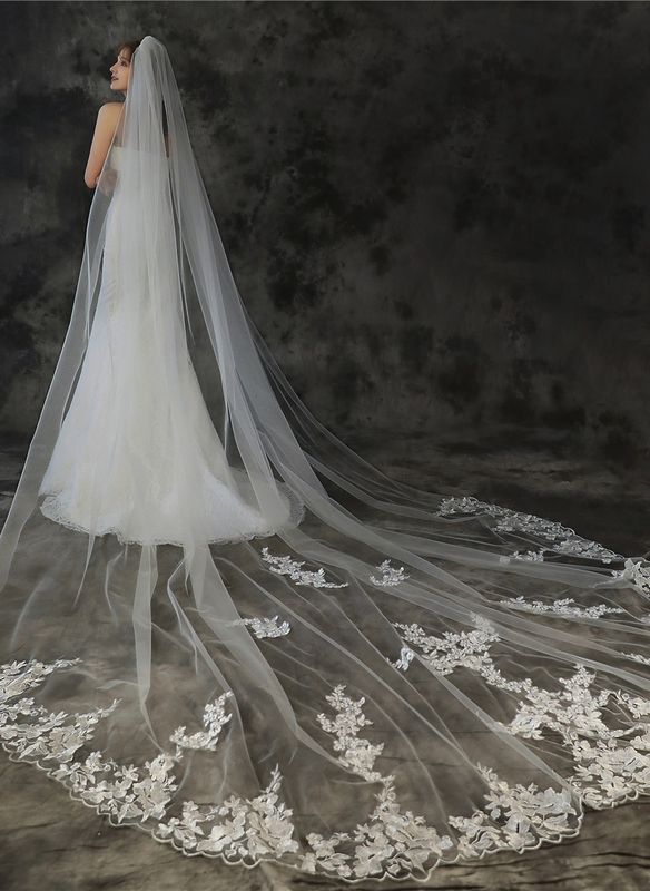 a woman wearing a wedding veil with white flowers on the bottom and long lace edge