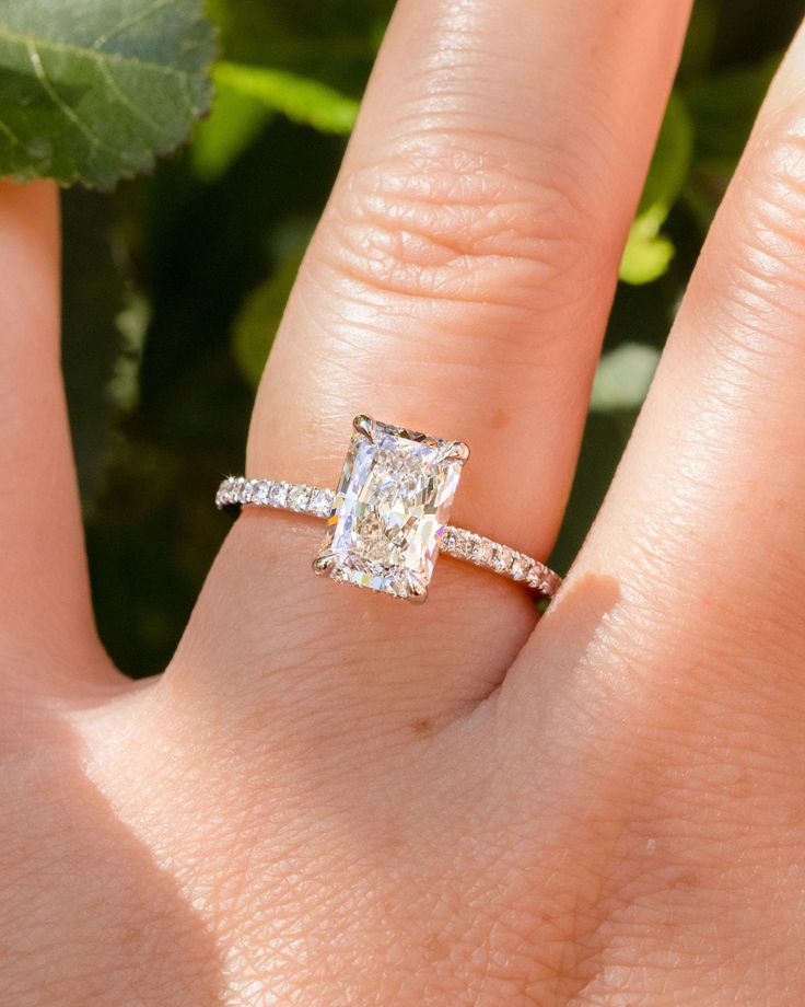 a woman's hand with a diamond ring on it and a leaf in the background