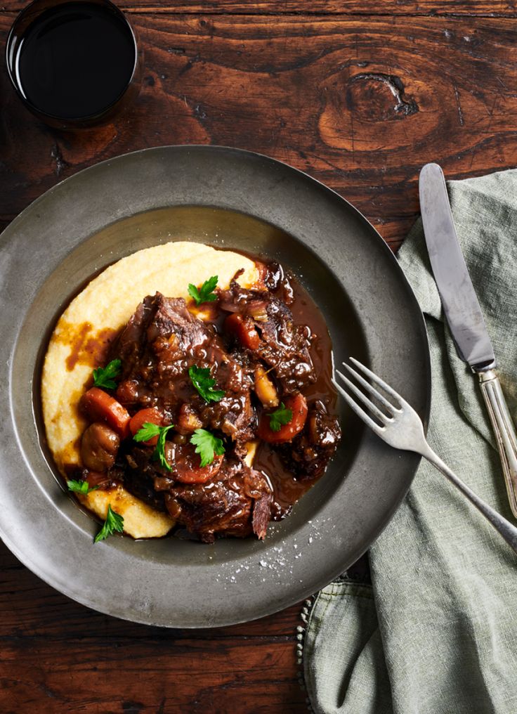 a plate with meat and potatoes on top of it next to a glass of wine