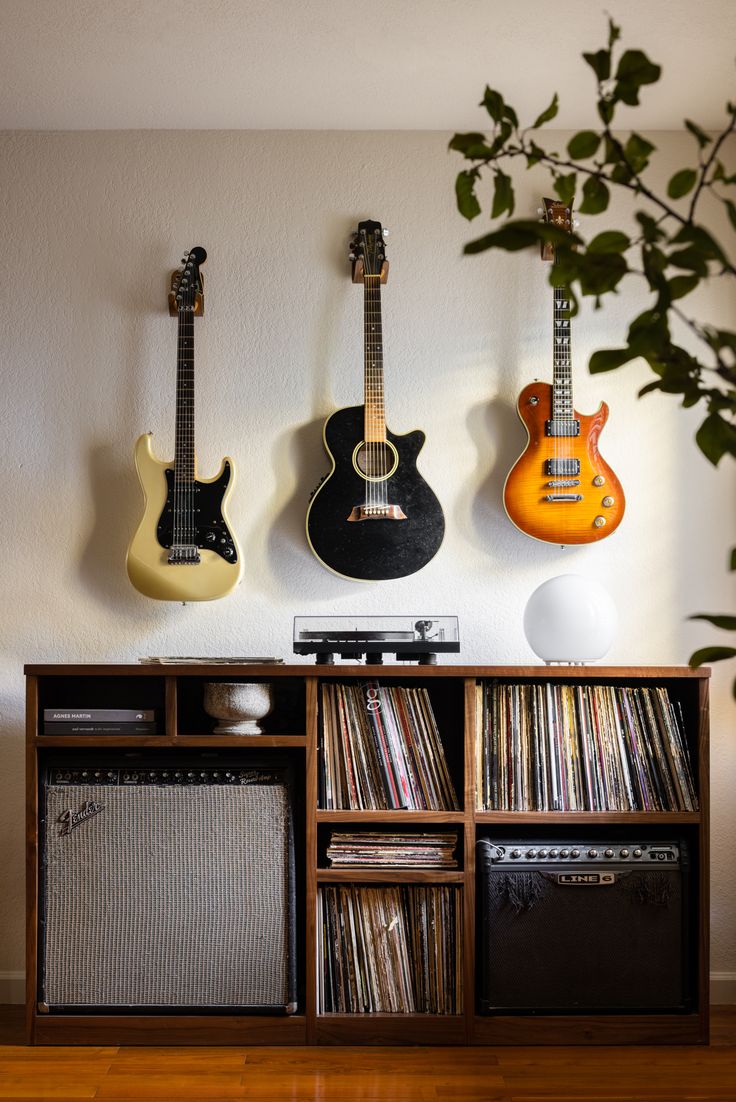 three guitars are hanging on the wall next to an old record player and stereo system