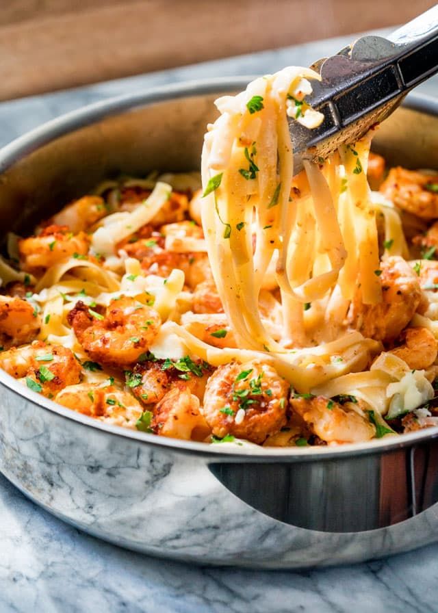 a ladle full of pasta with shrimp and parmesan cheese being lifted from the skillet