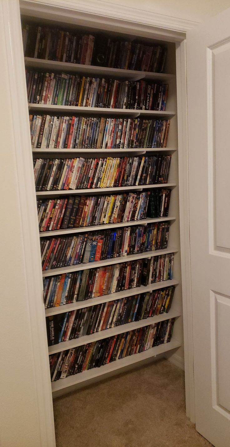 a white bookcase filled with lots of movies in a room next to a door