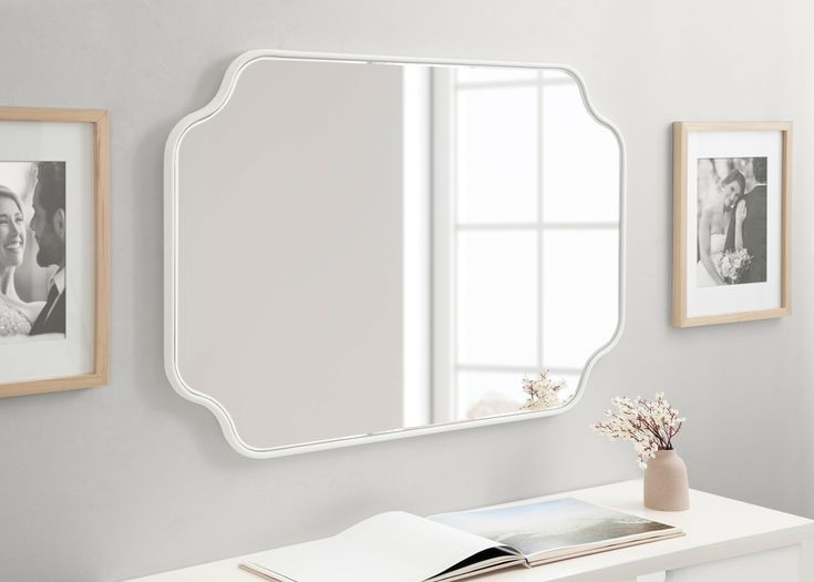 a white desk with a mirror and pictures on the wall above it, along with an open book