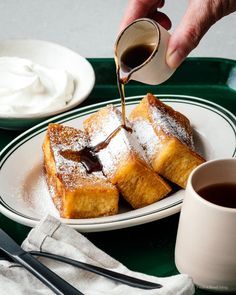 someone is pouring syrup on some french toast with powdered sugar and coffee in the foreground