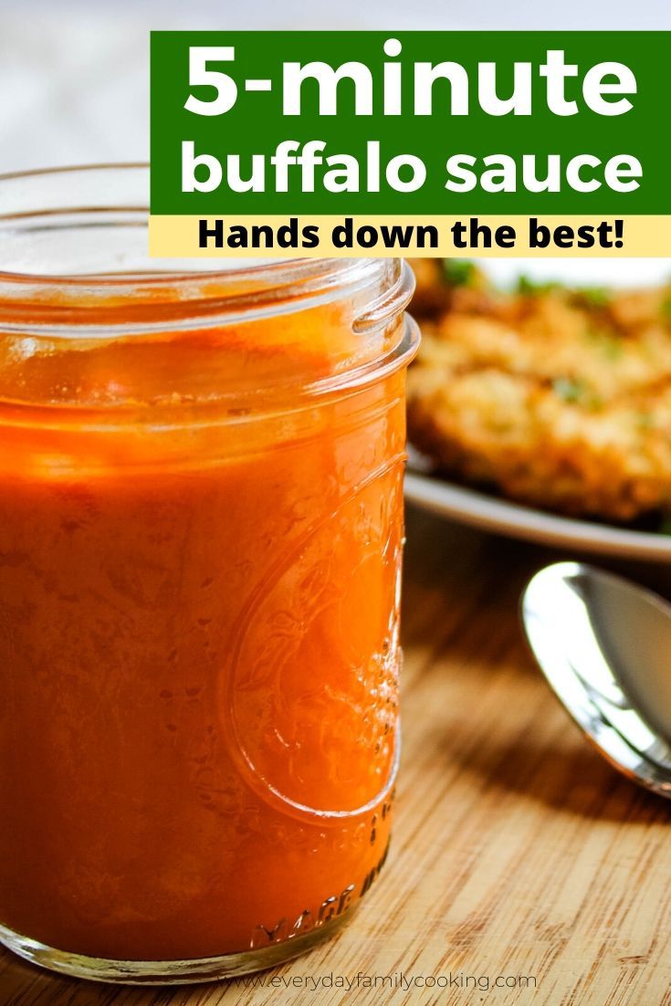 a jar filled with sauce sitting on top of a wooden table next to a spoon