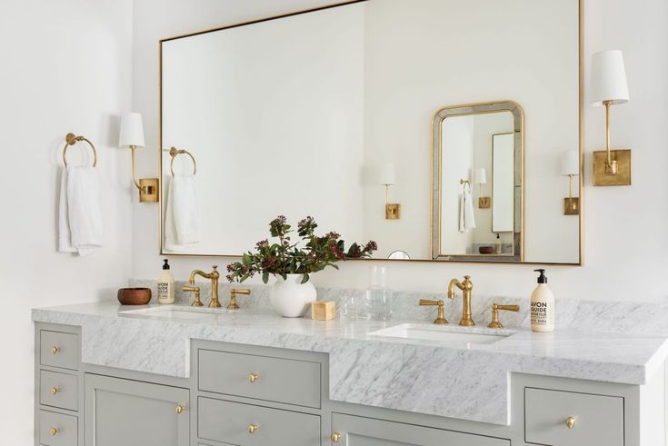 a bathroom vanity with two sinks and a large mirror above it, along with gold accents