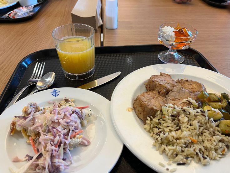 two white plates topped with meat and rice next to a glass of orange juice on a tray