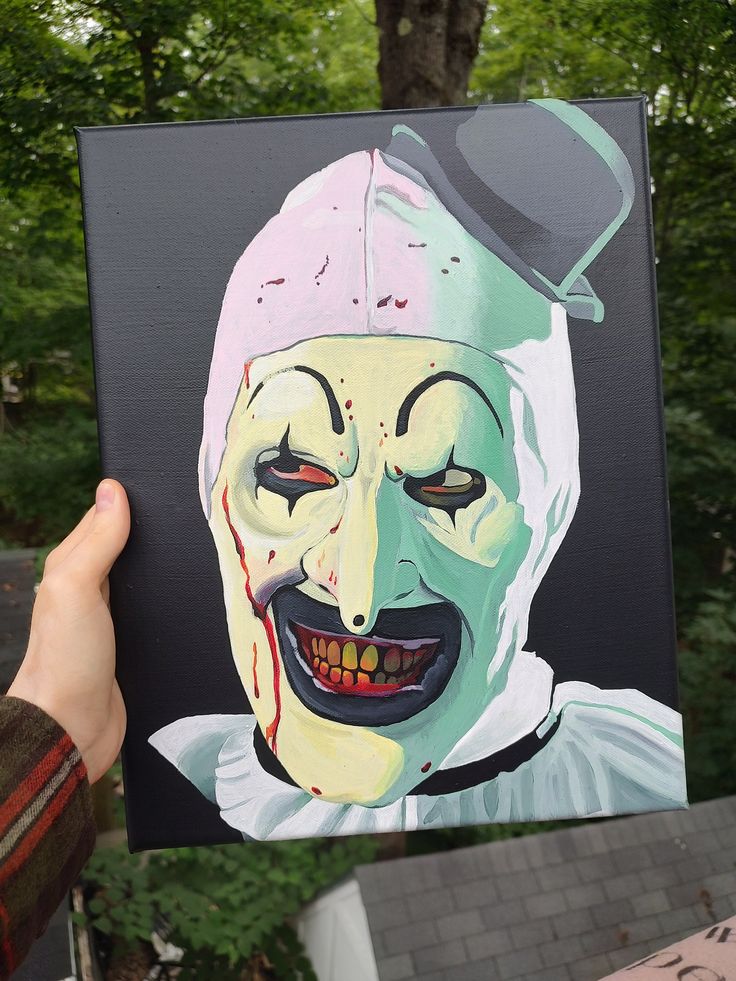 a person holding up a painting of a creepy clown