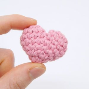 a pink crocheted heart is held in someone's hand