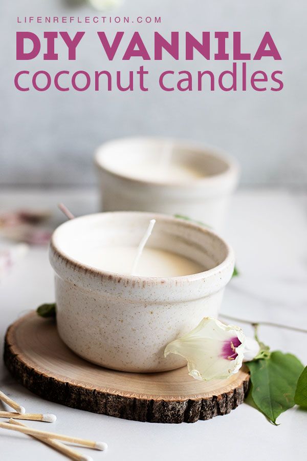 a white candle sitting on top of a wooden coaster next to some flowers and candles