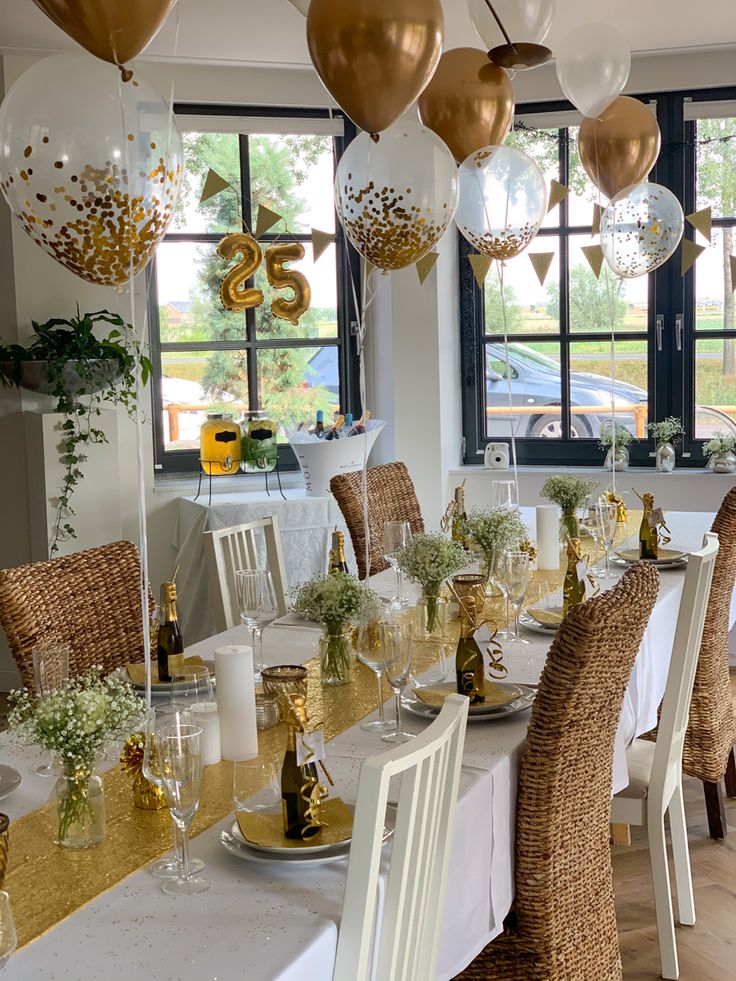 a table set for a party with gold and white balloons hanging from the ceiling over it