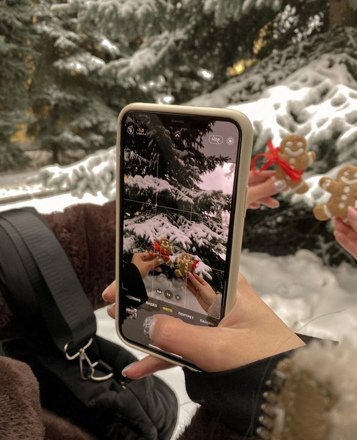 someone holding up their cell phone to take a photo in front of some snow covered trees