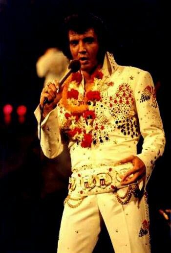 elvis presley singing into a microphone with his hand on his hip and wearing white pants