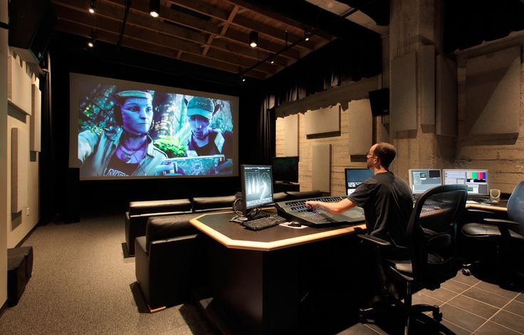 a man sitting at a desk in front of two computer monitors and a projector screen