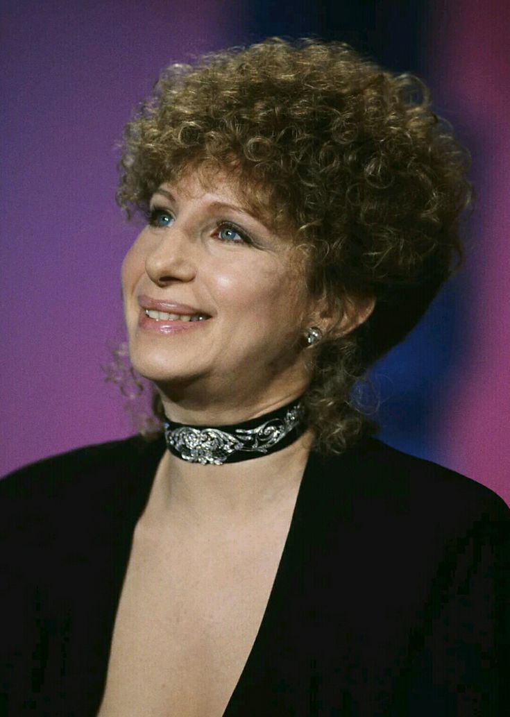 a woman with curly hair wearing a choker and black dress smiling at the camera