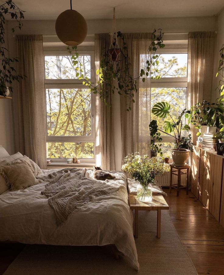 a bed room with a neatly made bed and lots of plants on the windowsill