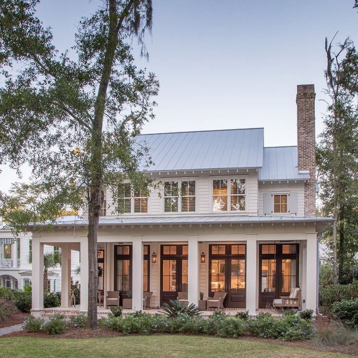 a white house with two porches on the front and side of it, surrounded by trees