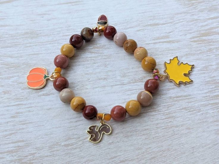 This beaded stretch charm bracelet features 4 enamel fall themed charms: 1/2 inch brown squirrel charm, 1 inch leaf charm, 1/2 inch acorn charm, 3/4 inch pumpkin Charm, along with 8mm mookaite round beads, 4mm faceted yellow/brown glass seed beads, and has a total measurement of 7 inches around. Brown Squirrel, Bracelets Handmade Beaded, Themed Jewelry, Leaf Charms, Cute Bracelets, Glass Seed Beads, Autumn Outfit, Blue Earrings, Autumn Theme