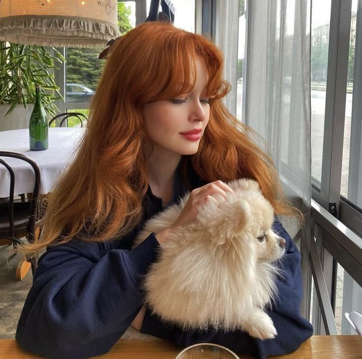 a woman sitting at a table holding a small white dog