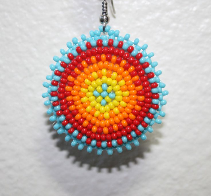 a colorful beaded object hanging from a hook on a white wall in the shape of a circle