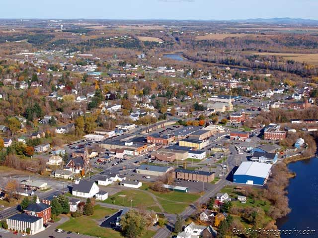 an aerial view of a small town with lots of trees in the foreground and a body of water